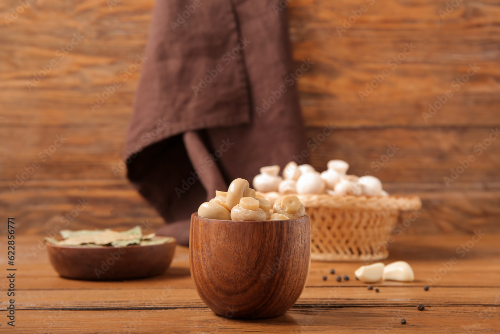 Bowl with canned mushrooms on wooden background