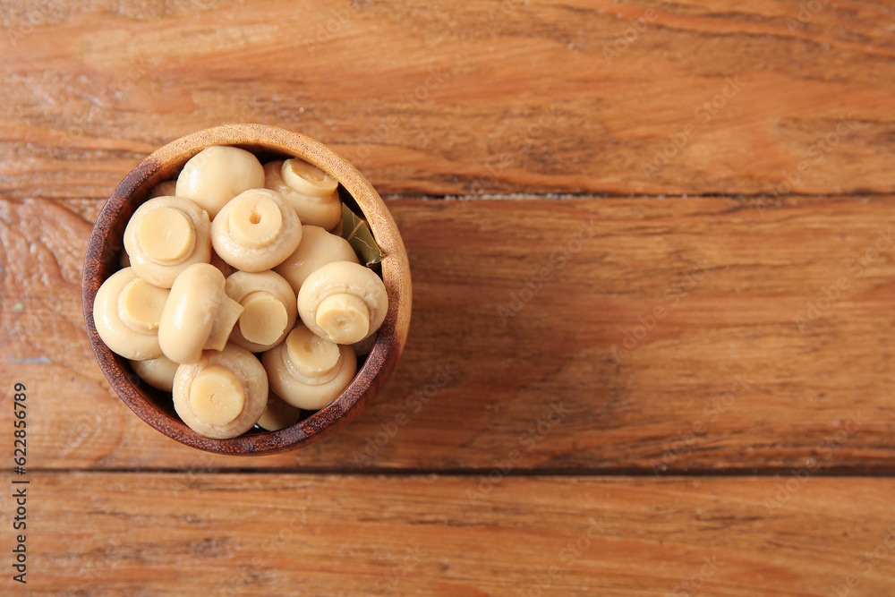 Bowl with canned mushrooms on wooden background