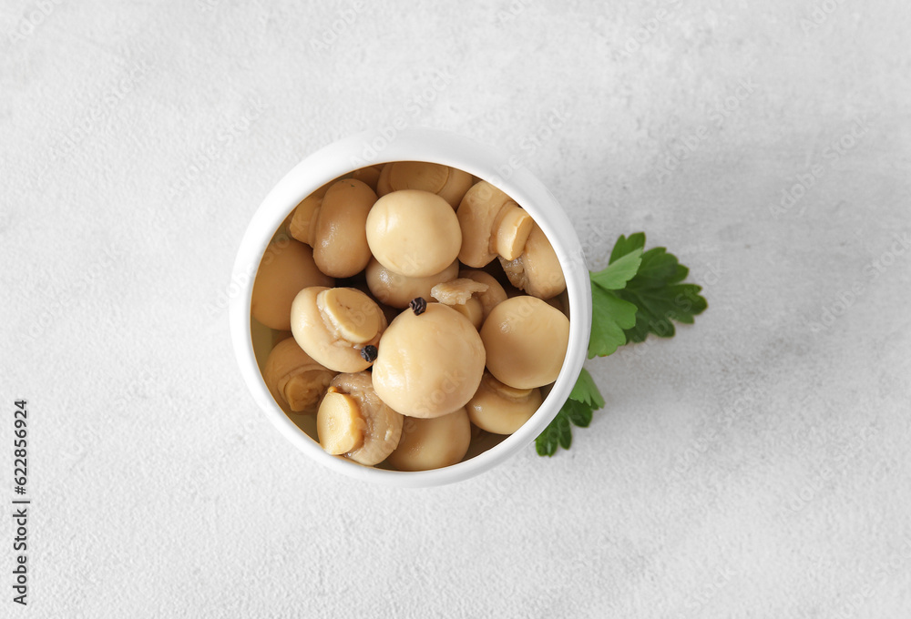 Bowl with canned mushrooms on light background