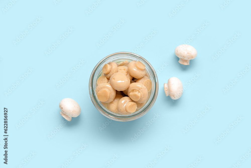 Jar with canned mushrooms on blue background