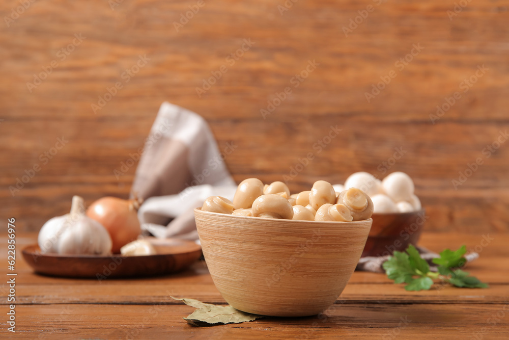 Bowl with canned mushrooms on wooden background