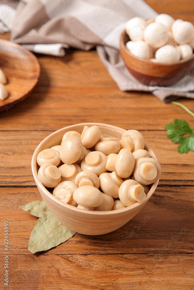 Bowl with canned mushrooms on wooden background