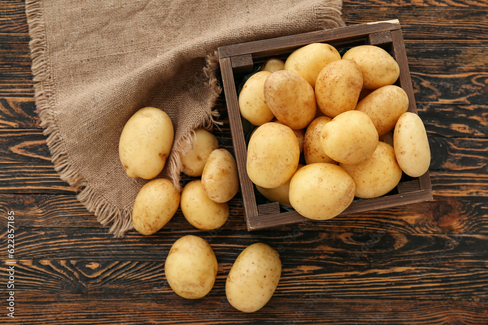 Box with raw potatoes on wooden background