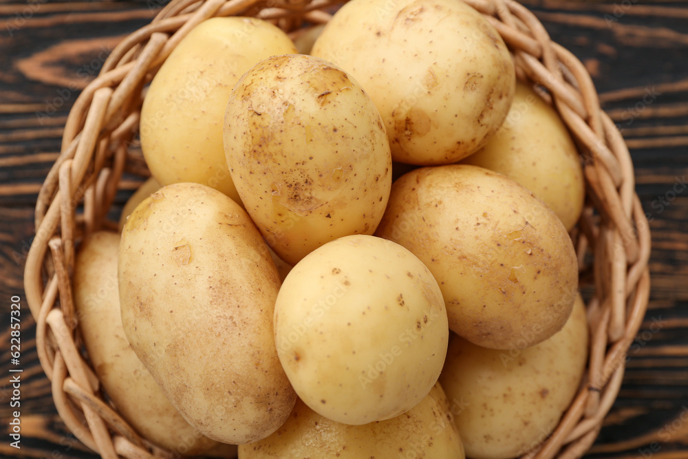 Wicker bowl with raw potatoes on wooden background, closeup