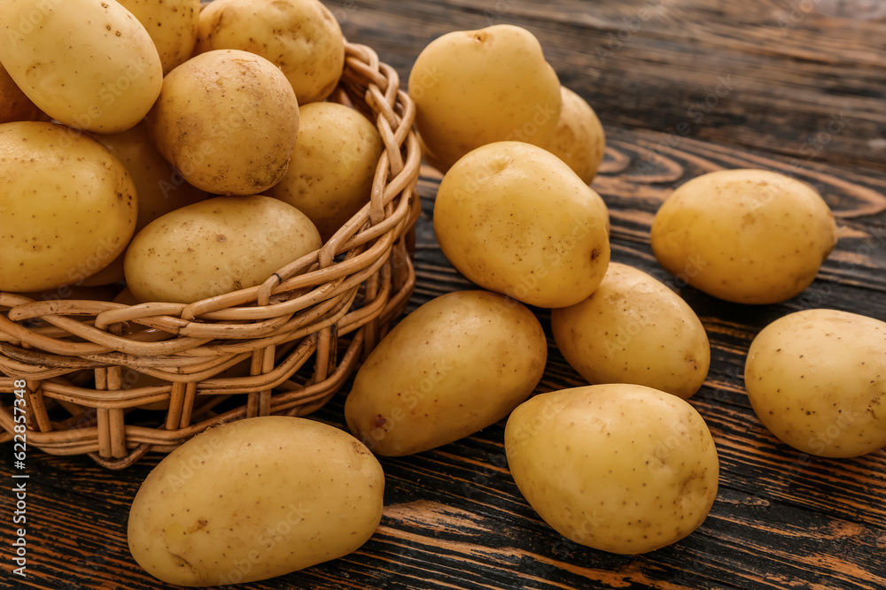 Wicker bowl with raw potatoes on wooden background