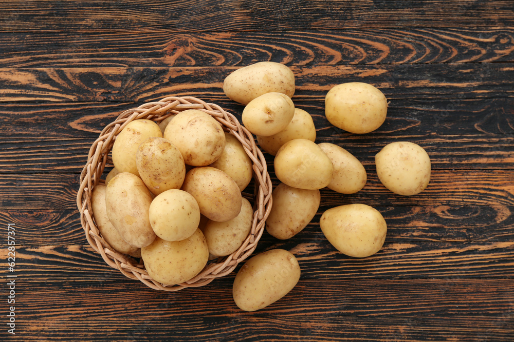 Wicker bowl with raw potatoes on wooden background