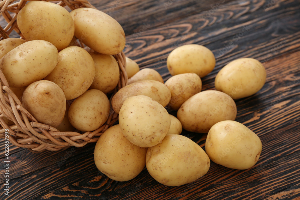 Wicker bowl with raw potatoes on wooden background