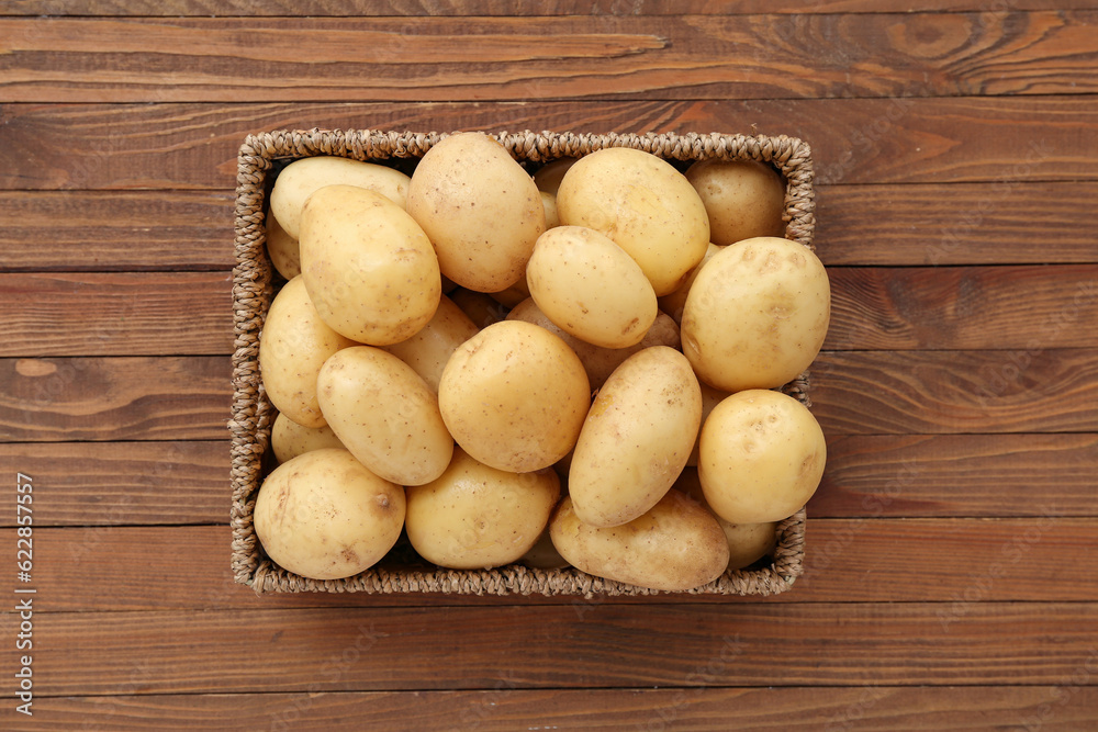 Wicker box with raw potatoes on wooden background