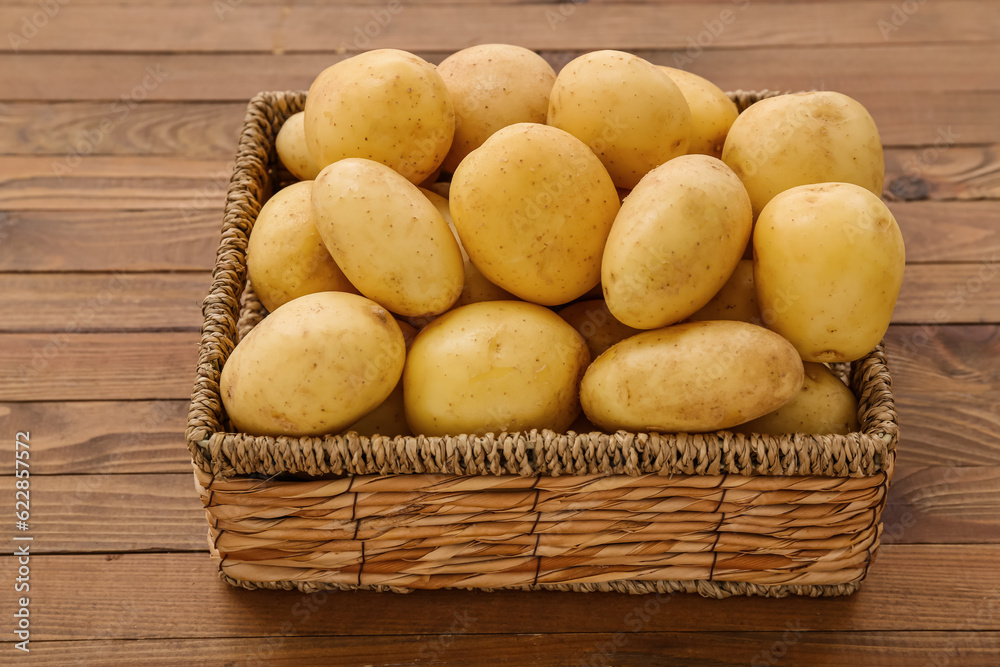 Wicker box with raw potatoes on wooden background