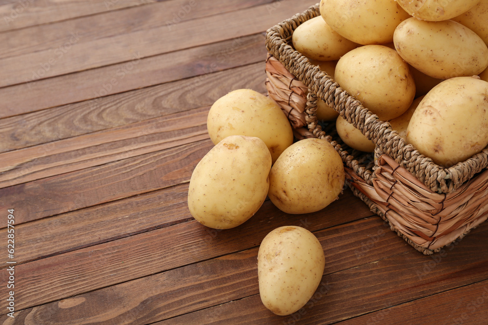 Wicker box with raw potatoes on wooden background