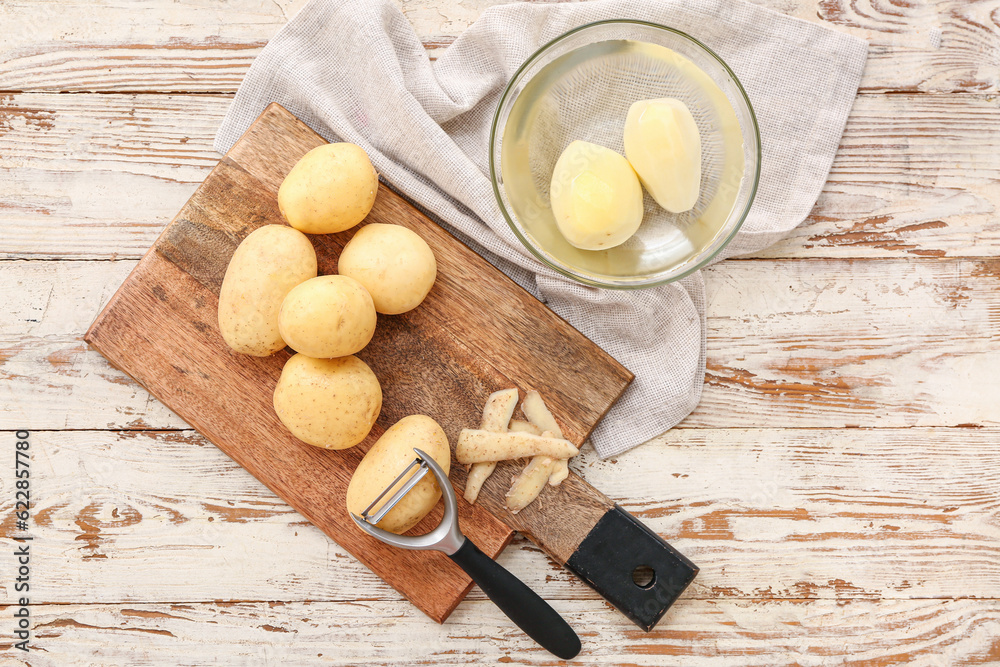 Board and bowl with raw potatoes on white wooden background