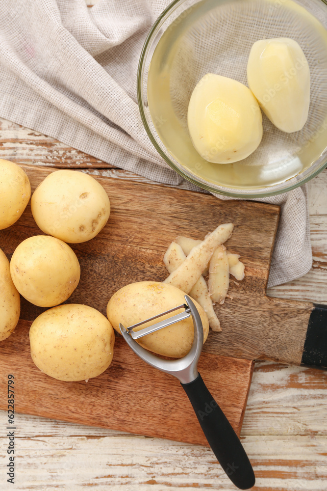 Board and bowl with raw potatoes on white wooden background