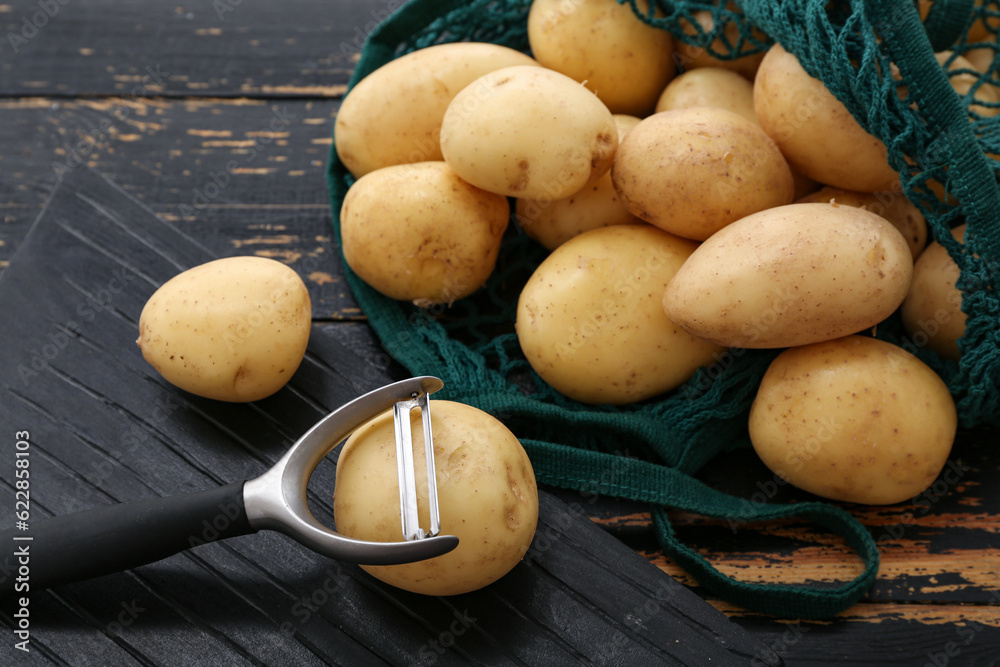 Board and string bag with raw potatoes on black wooden background