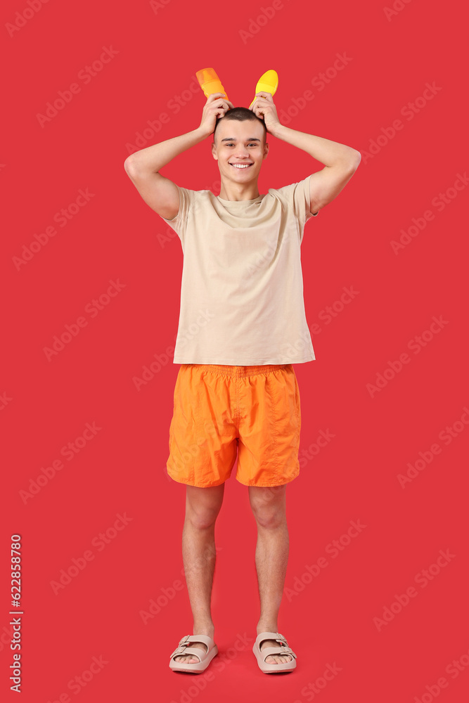 Happy young man with bottles of sunscreen cream on red background