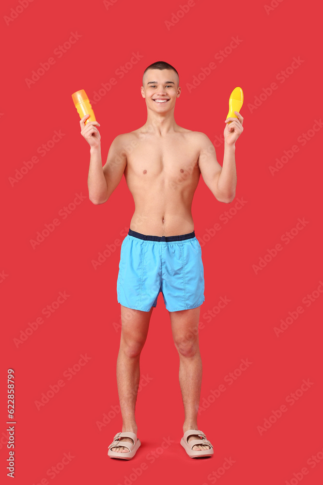 Happy young man with bottles of sunscreen cream on red background