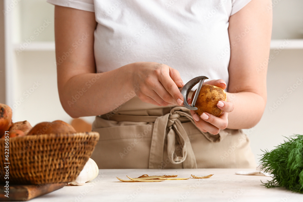 Woman peeling raw potato at table in kitchen