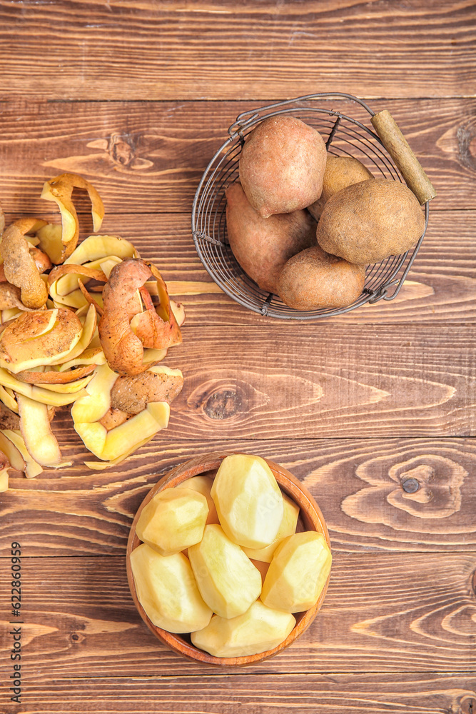 Bowl and basket with raw potatoes on wooden background