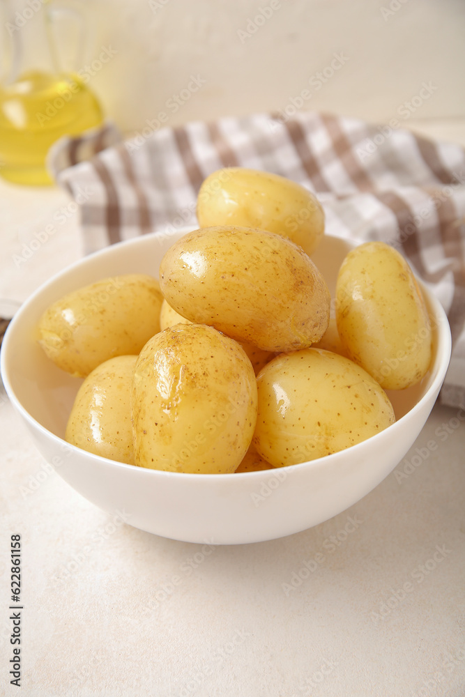 Bowl with raw potatoes on light background