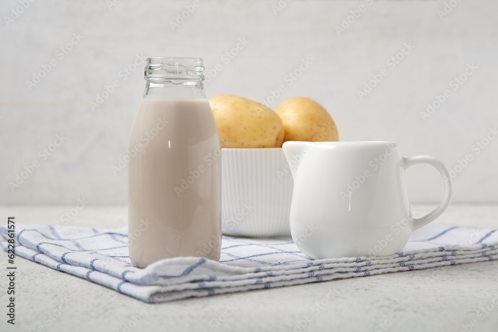 Bottle and jug of tasty potato milk on light background