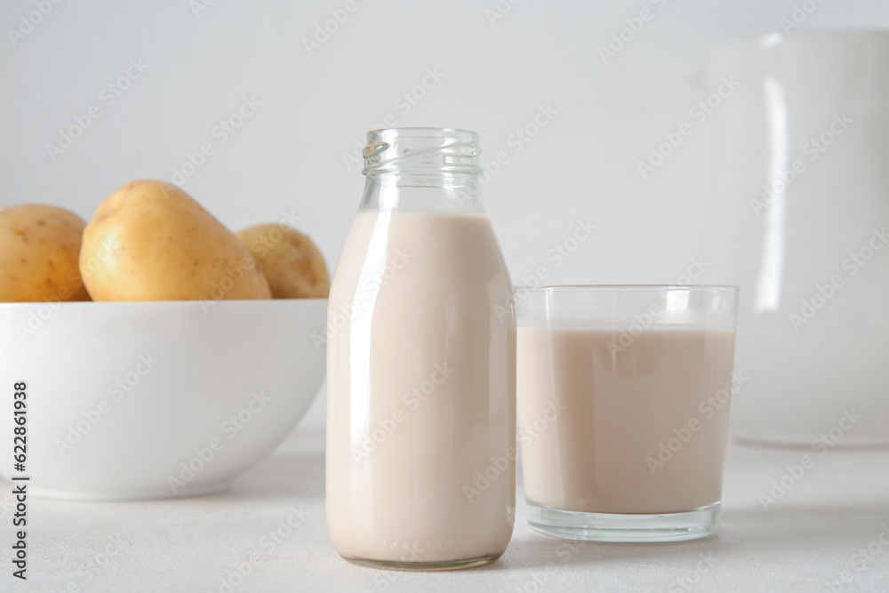 Bottle and glass of tasty potato milk on light background