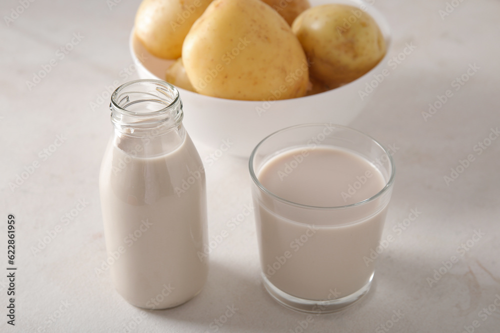 Bottle and glass of tasty potato milk on light background