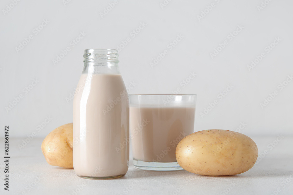 Bottle and glass of tasty potato milk on light background