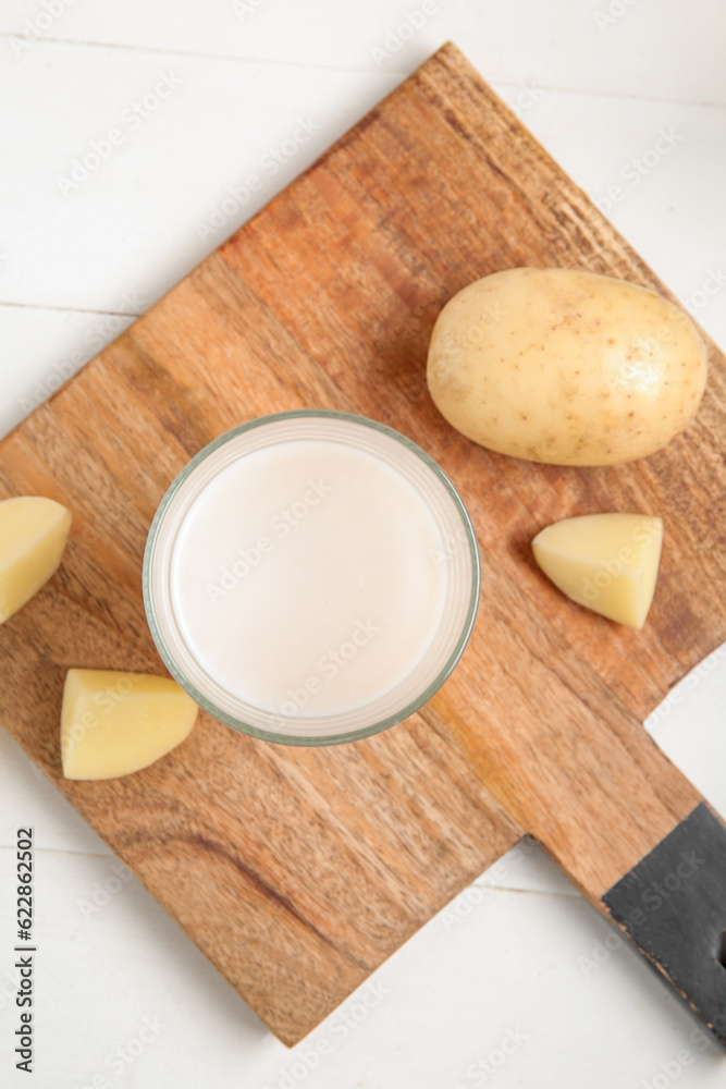 Glass of tasty potato milk on white wooden background