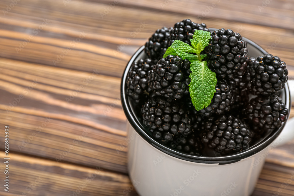 Cup with fresh blackberry on wooden background, closeup