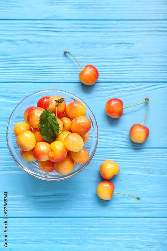 Bowl with fresh yellow cherry on blue wooden background