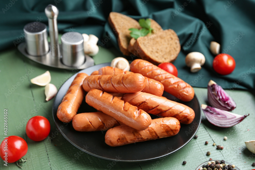 Plate with tasty grilled sausages and vegetables on green wooden table, closeup