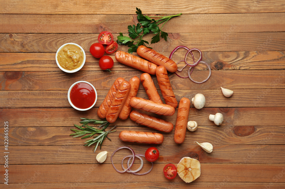 Tasty grilled sausages, vegetables, herbs and sauces on wooden table