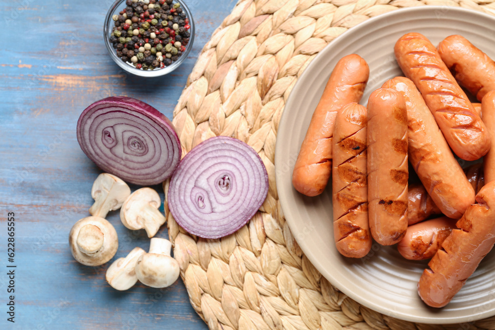 Plate with tasty sausages, onions and mushrooms on blue wooden table