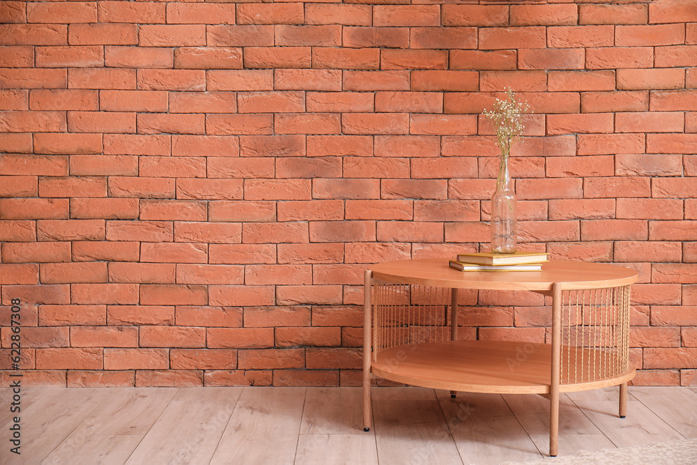 Wooden coffee table with books and vase near brown brick wall