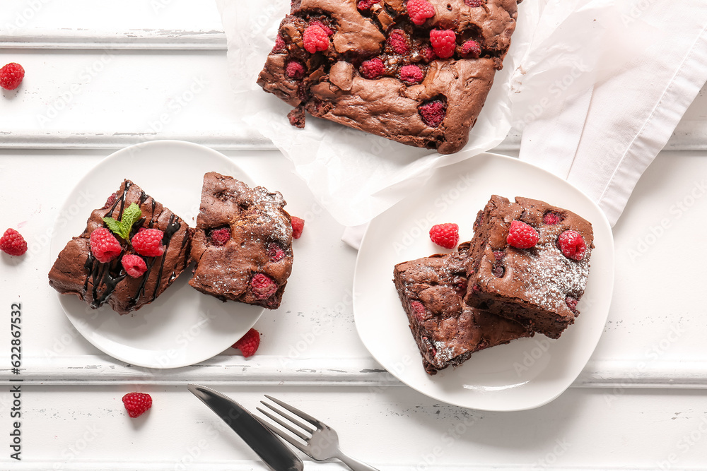 Plates and baking paper with raspberry chocolate brownie on white background