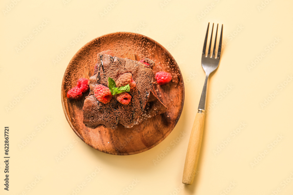 Wooden plate with pieces of raspberry chocolate brownie on orange background