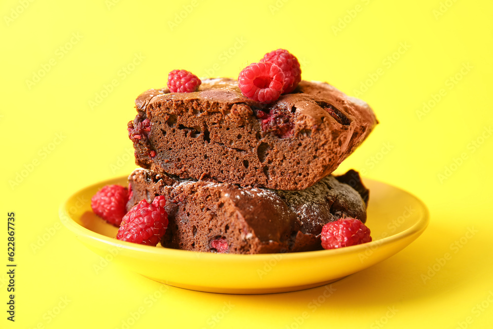 Plate with pieces of raspberry chocolate brownie on yellow background