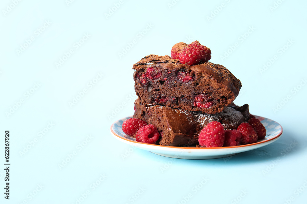 Plate with pieces of raspberry chocolate brownie on blue background