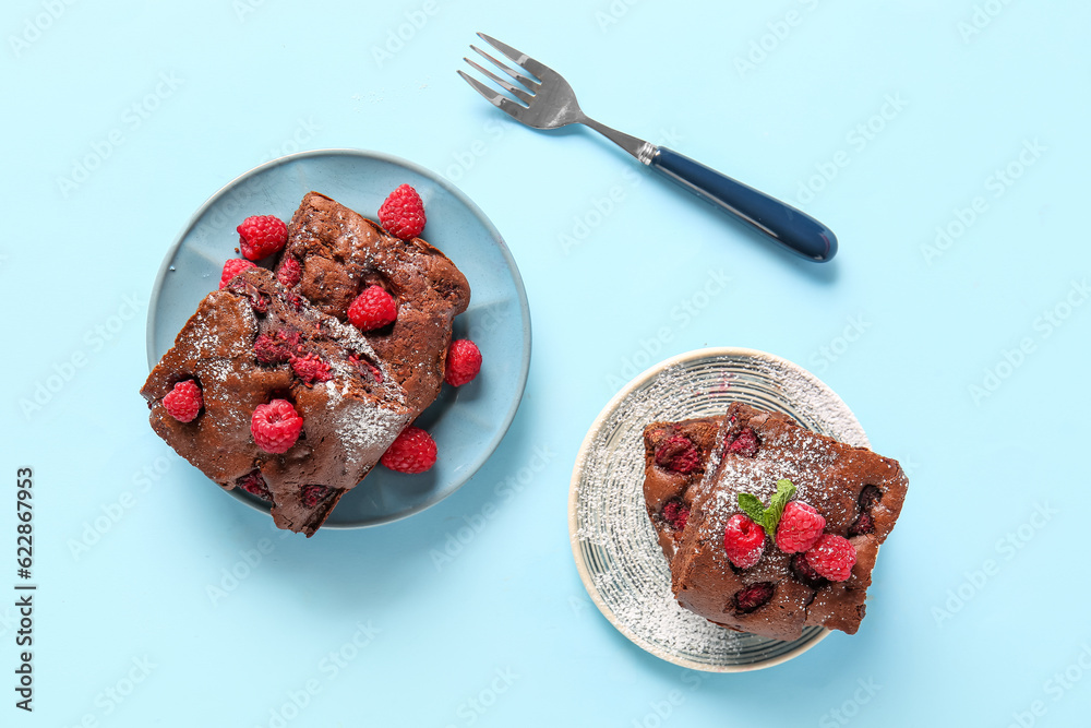 Plates with pieces of raspberry chocolate brownie on blue background