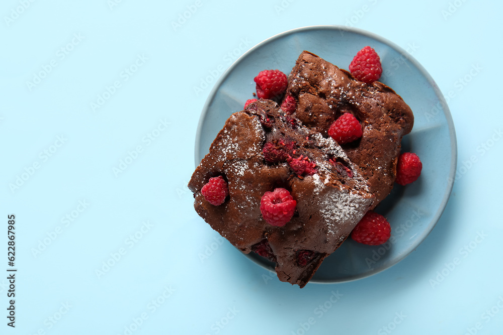 Plate with pieces of raspberry chocolate brownie on blue background