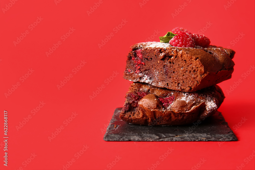 Board with pieces of raspberry chocolate brownie on red background