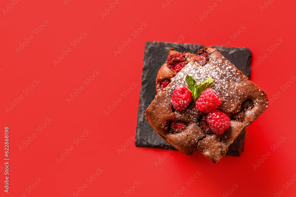 Board with pieces of raspberry chocolate brownie on red background