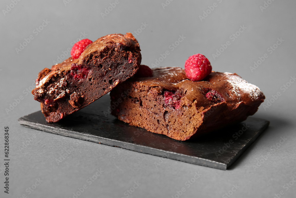 Board with pieces of raspberry chocolate brownie on grey background