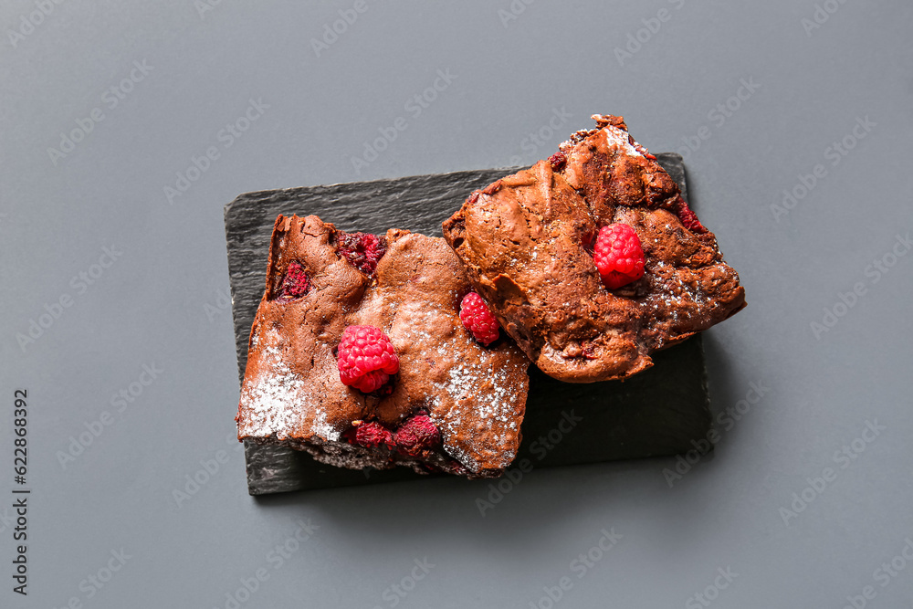 Board with pieces of raspberry chocolate brownie on grey background