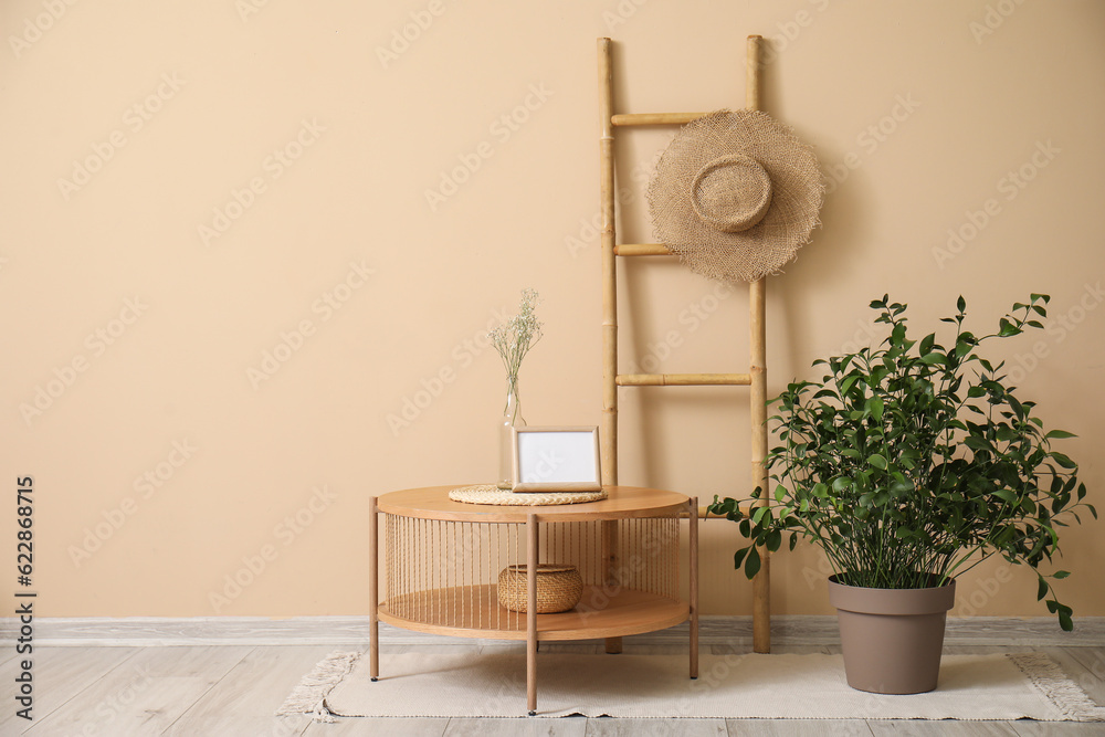 Wooden coffee table with blank frame and houseplant near beige wall