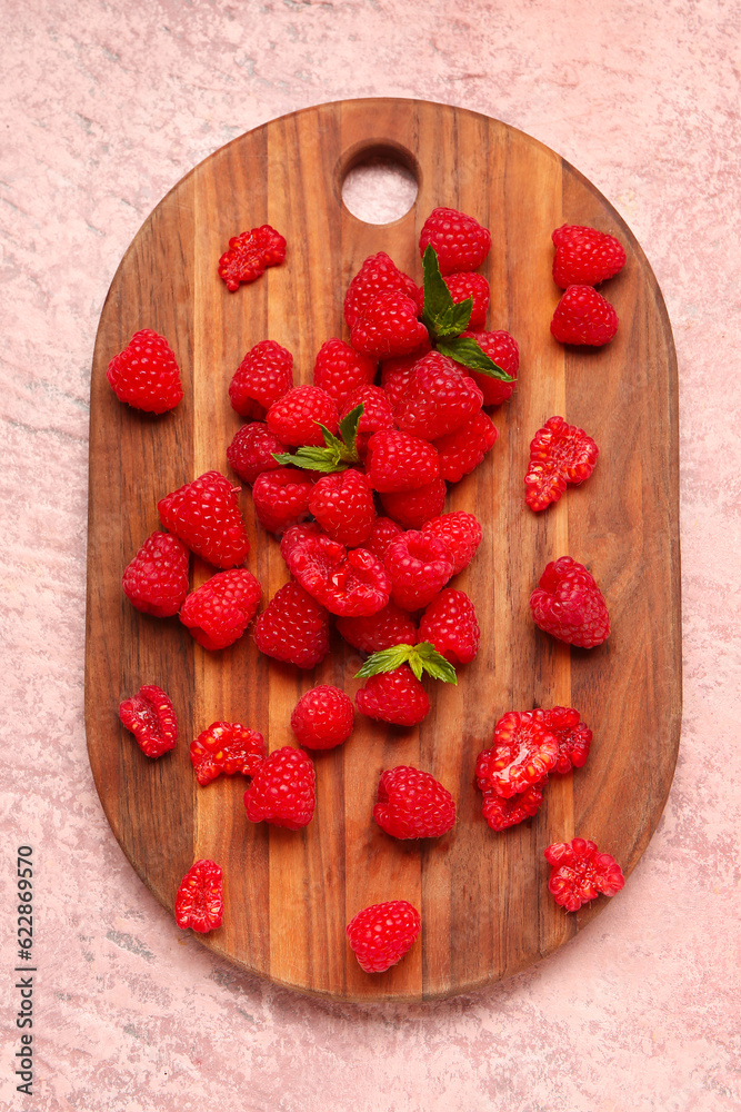 Wooden board with fresh raspberries and mint on pink background