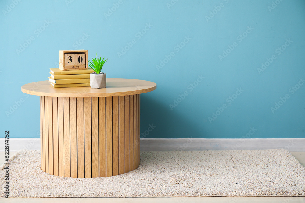 Coffee table with books, cube calendar and houseplant near blue wall