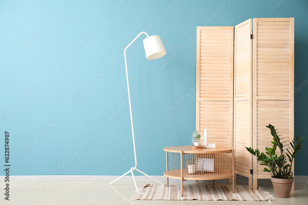 Coffee table with decor, houseplant and folding screen near blue wall