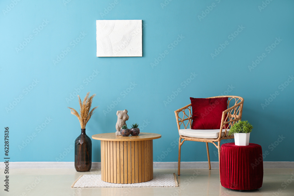 Coffee table, armchair and red pouf near blue wall