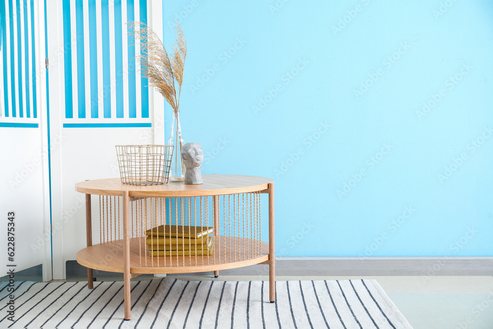 Coffee table with pampas grass, books and folding screen near blue wall