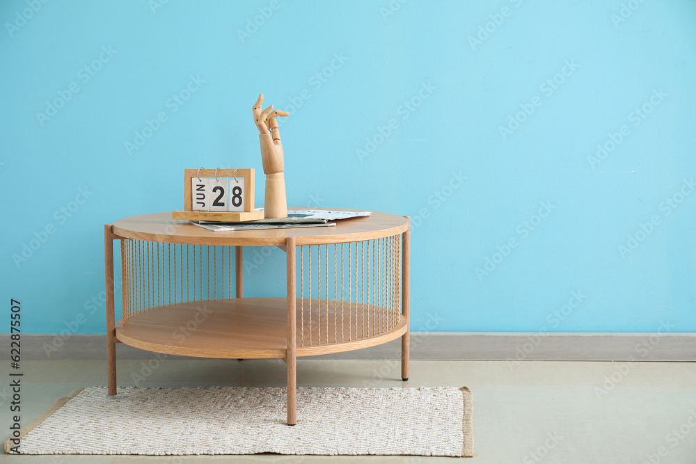 Coffee table with wooden hand and cube calendar near blue wall